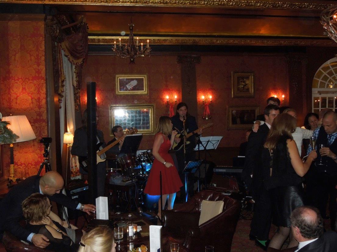 Claire Bender singing in a red dress at a live restaurant event with seated guests